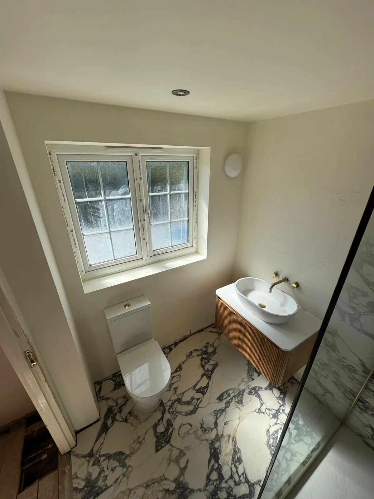 A countertop basin with a gold tap on a fluted wooden vanity, with a marble effect floor