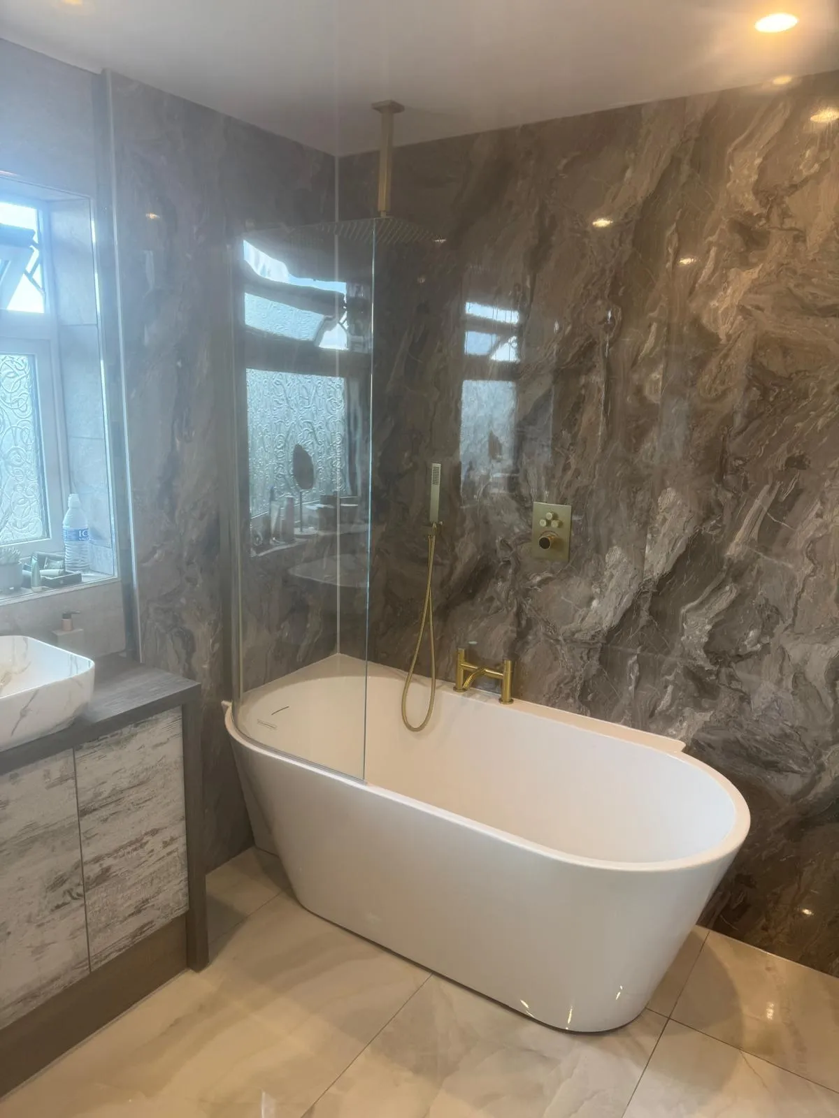 A freestanding bath with gold taps against a marble effect wall