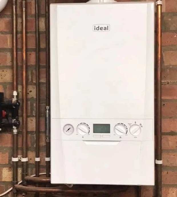 A white Ideal boiler on a red brick wall with neatly run copper pipework