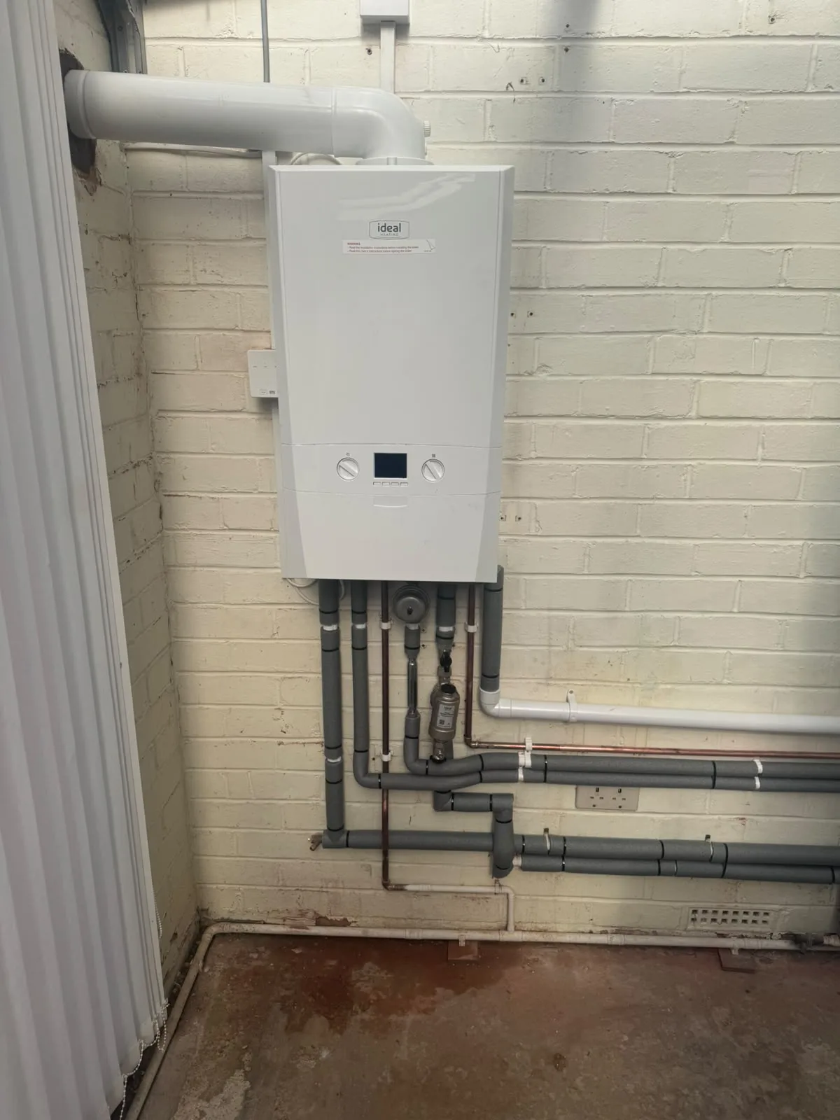A new Ideal boiler on a painted brick wall with insulated pipework below