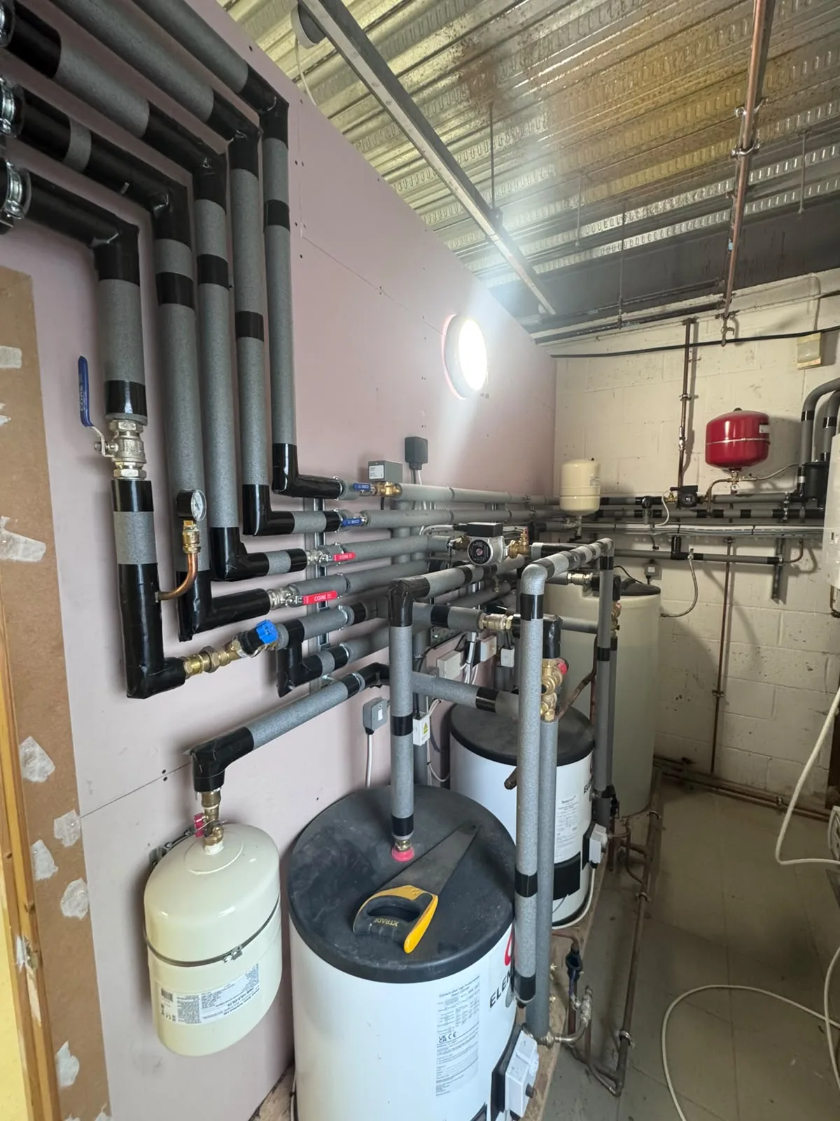 A plant room with hot water cylinders and insulated pipework with valves