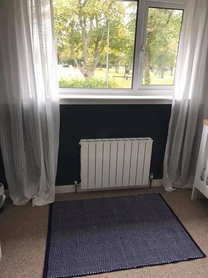 A white column radiator under a bedroom window with sheer curtains