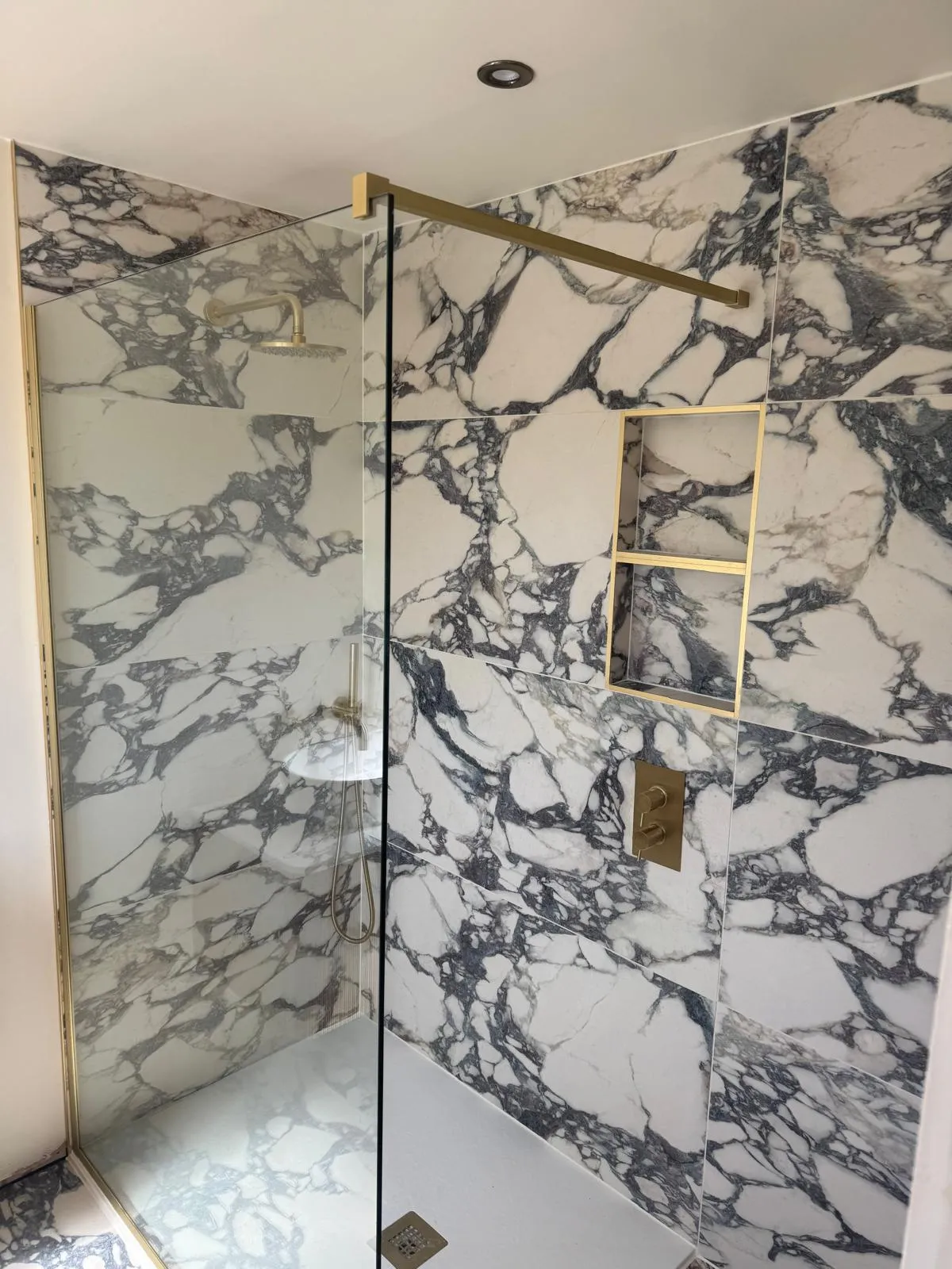 A walk in shower with marble effect tiles and gold fittings