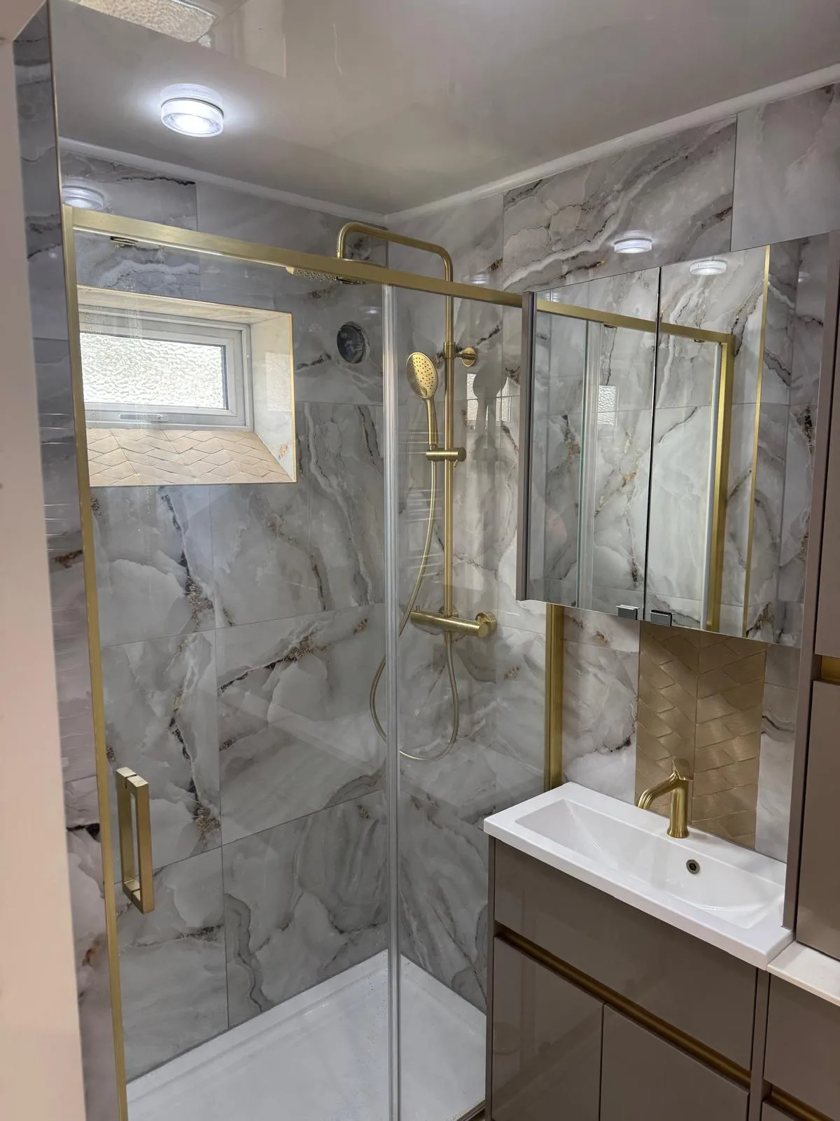 A shower room with marble effect walls and gold fittings
