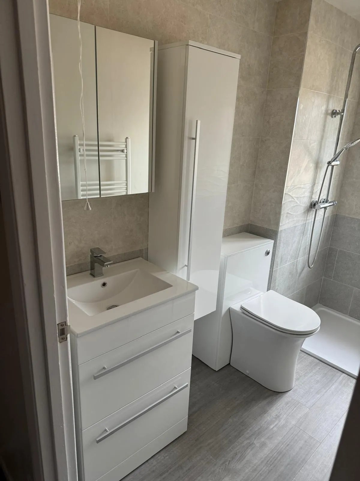 A shower room with a white vanity unit, tall cupboard and a walk in shower